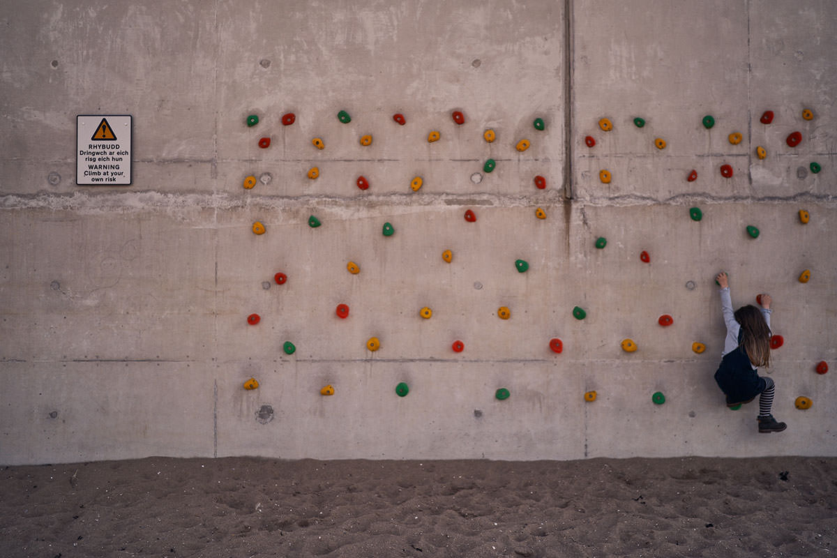young child climing a climbing wall on the beach