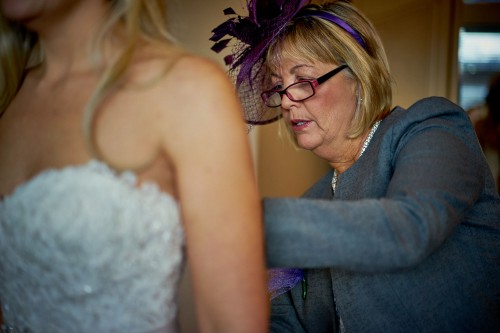 brides mother helping bride into her dress
