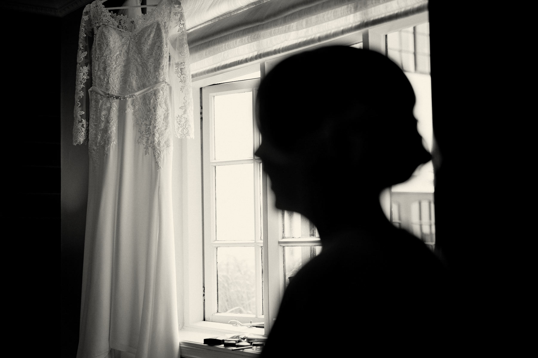 Silhouette of bride with wedding dress hanging in the window