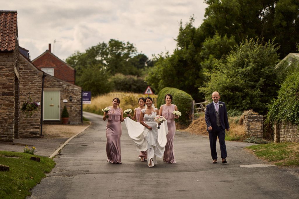 wedding party walking through Yorkshire village on their way to the church